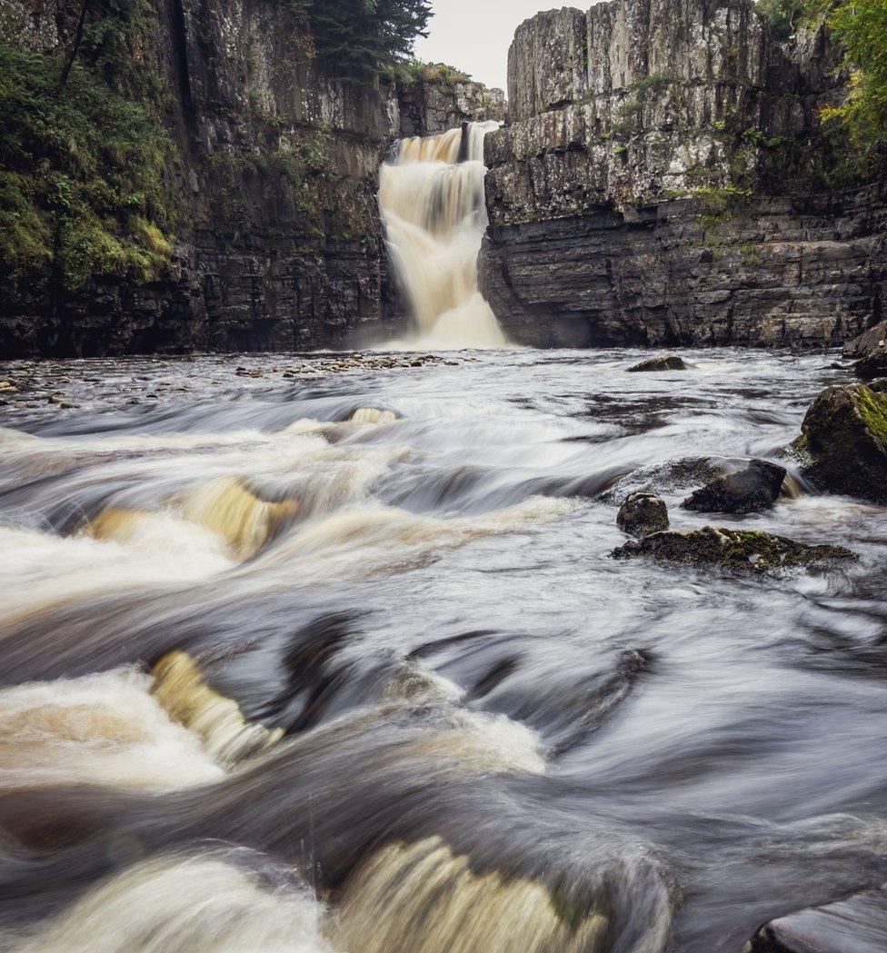 Water rushing over rocks with a waterfall in the background