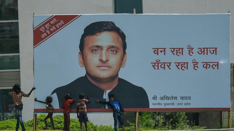 Young Indian children play around a hoarding featuring an image of Uttar Pradesh Chief Minister Akhilesh Yadav in Greater Noida on April 12, 2016.