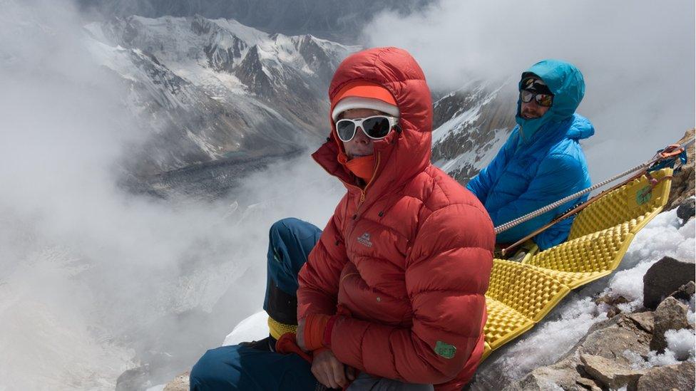 Two men sit on the edge of the mountain overlooking a valley