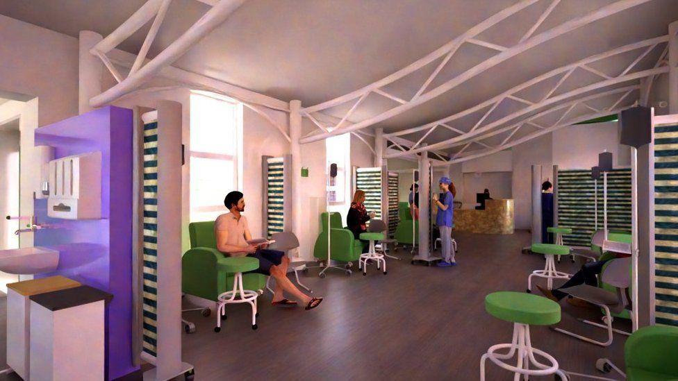 Patients sit on green seats in white room with nursing staff at back of room and sink and bins to the front left