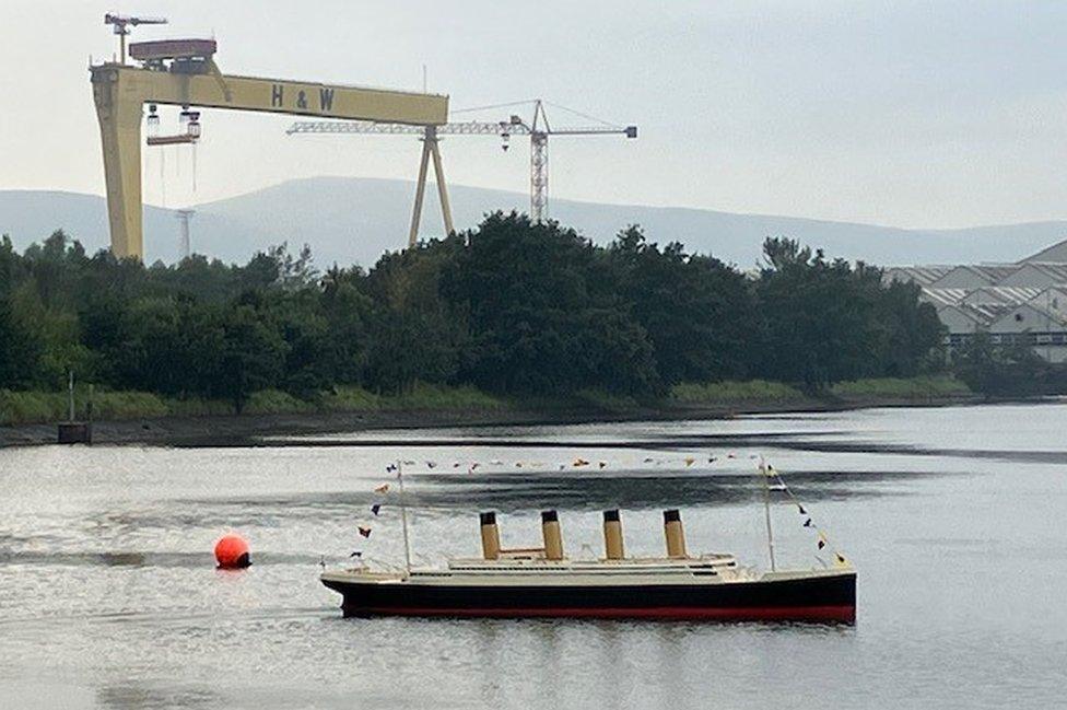 The model of Titanic on the waters at Belfast Lough, with the Harland & Wolff shipyard cranes in the background