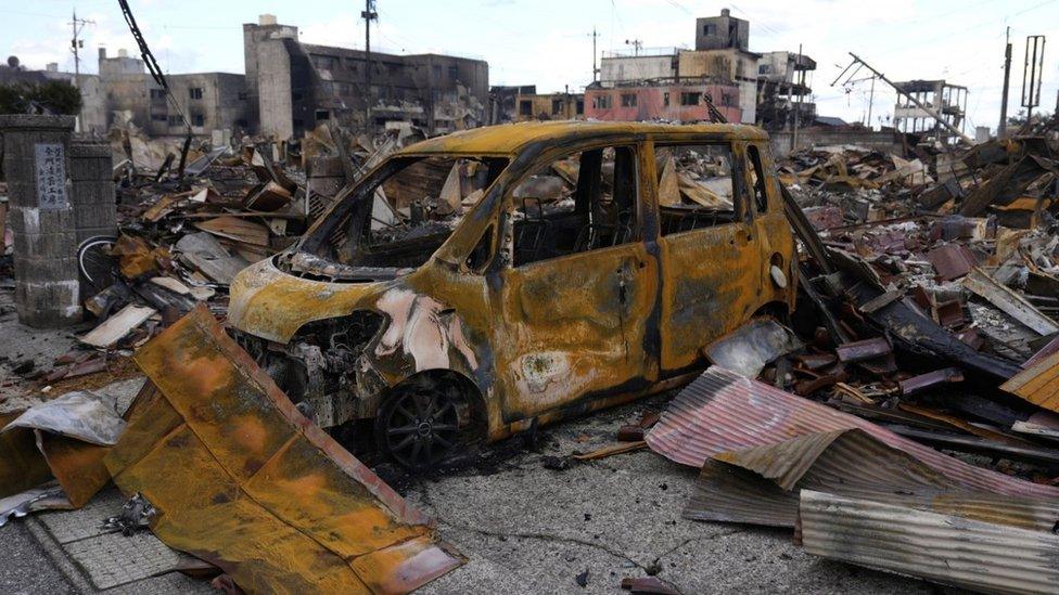 A view of the burnt remains of a vehicle and building structures following an earthquake in Wajima, Japan