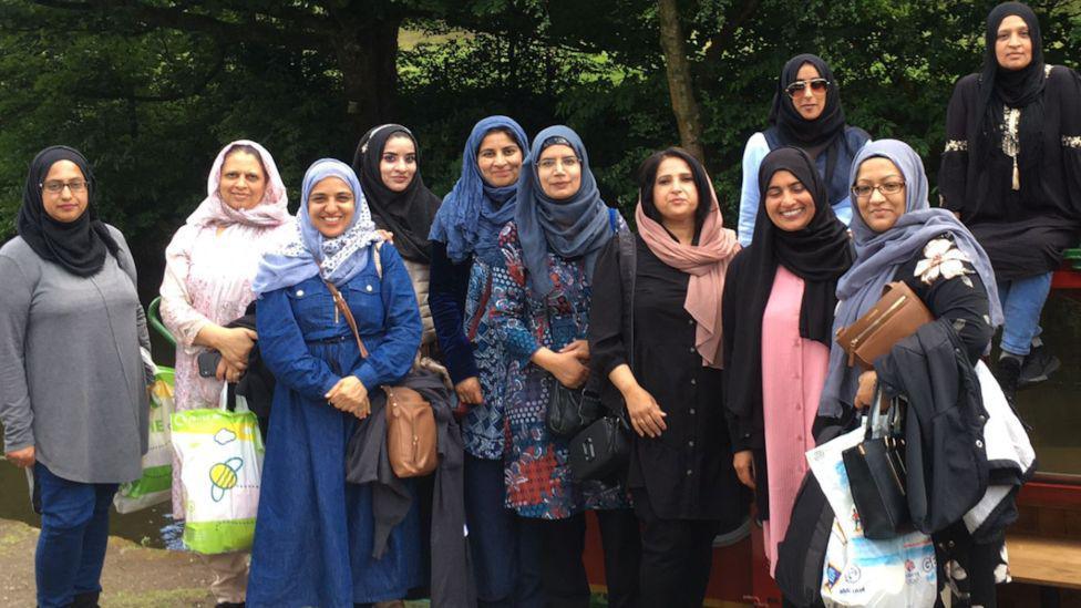 Eleven of the women in the group, standing and smiling, all wearing hijabs 