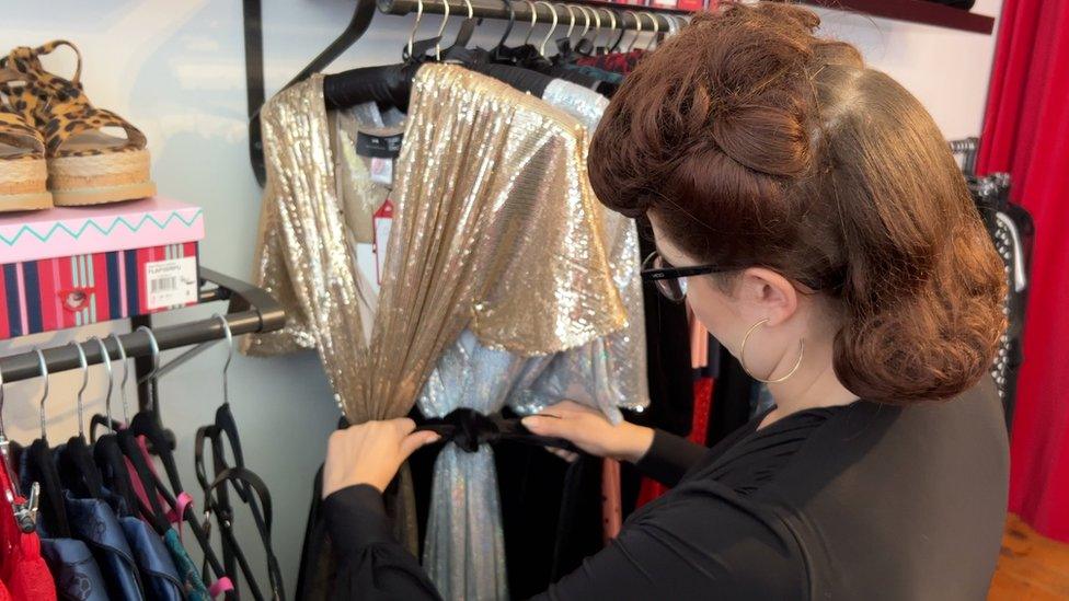 Sarah Wingrove facing away from camera arranging dresses on a clothes rail