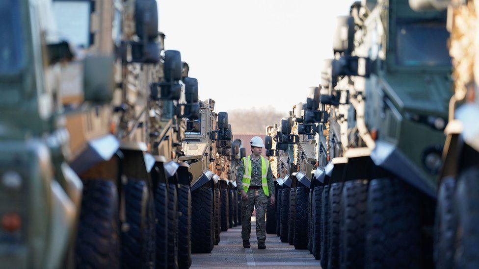 Two lines of army vehicles in a long queue with a man in the centre of both wearing arm trousers and a high-vis jacket.