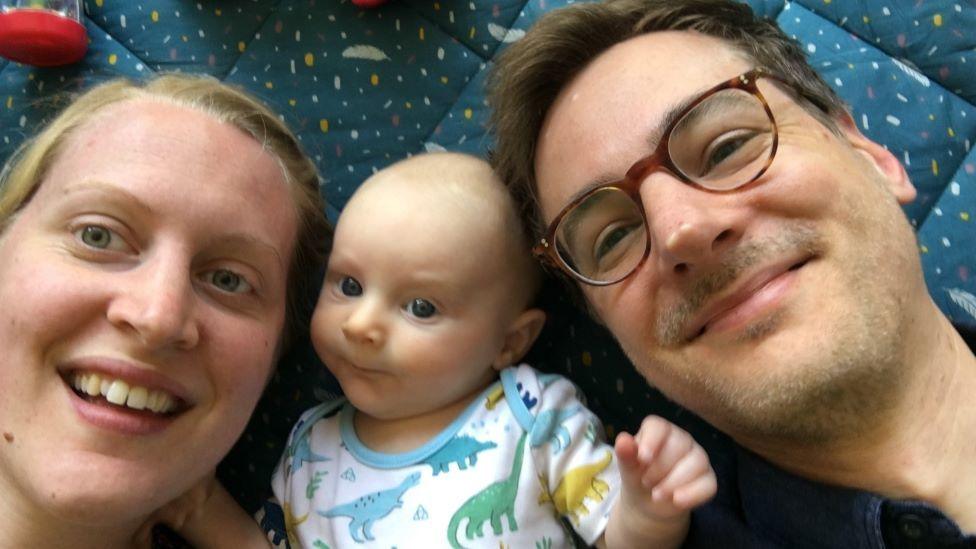 A woman, man and baby lie on the floor and take a selfie