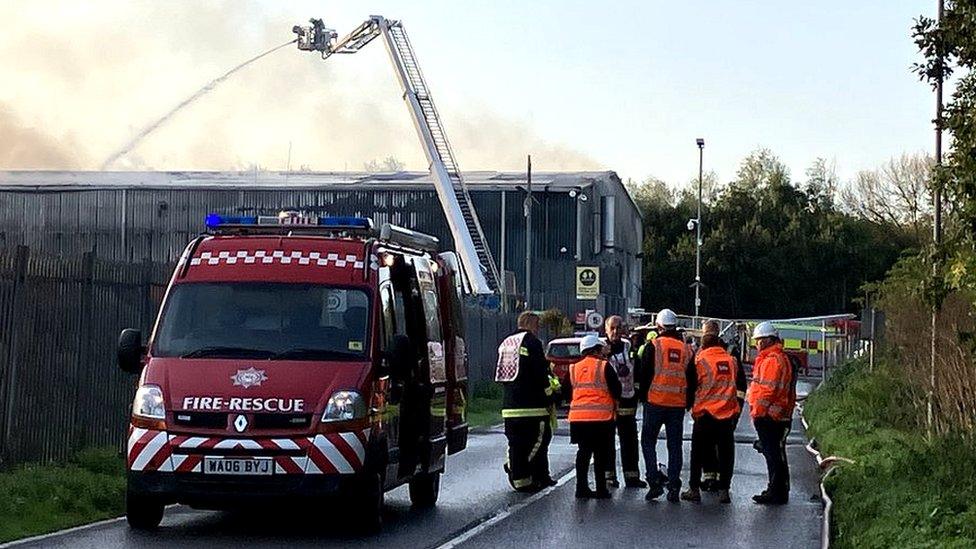 Firefighters in front of a large building with smoke rising from it