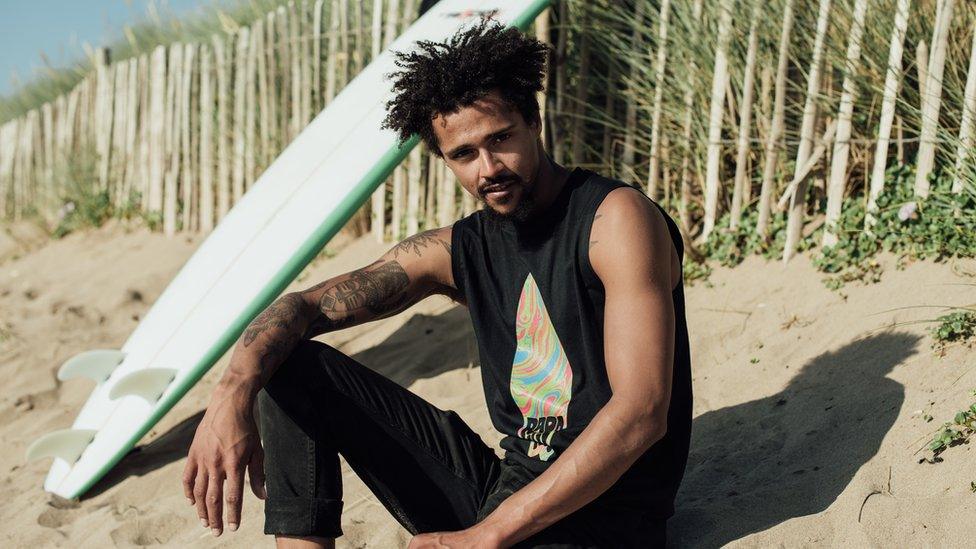 Jarrakeh modelling clothes on a beach in front of a surfboard