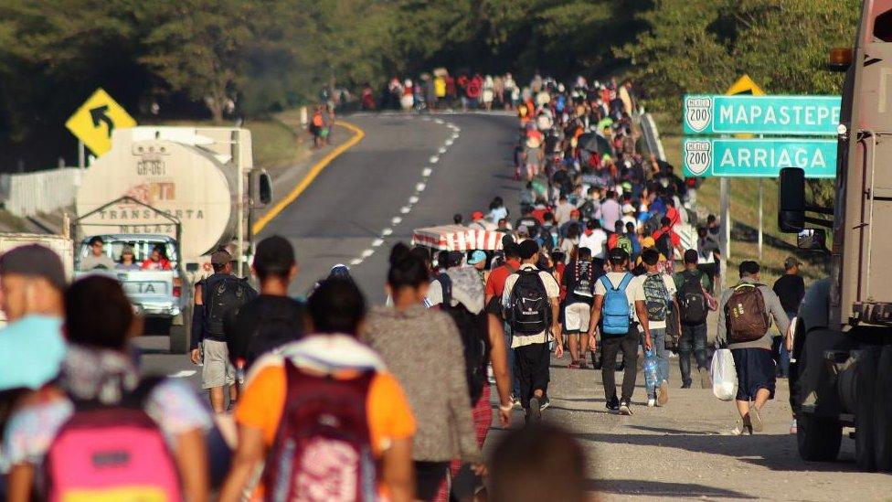 A wide shot showing a crowd of people walking alongside a road in Mexico