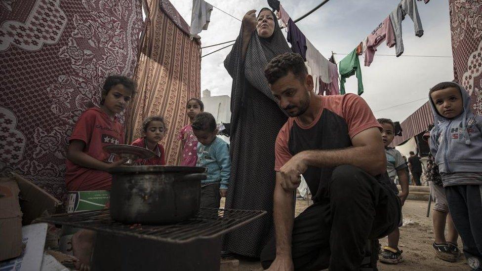 People cook food inside a tent complex in a tent camp