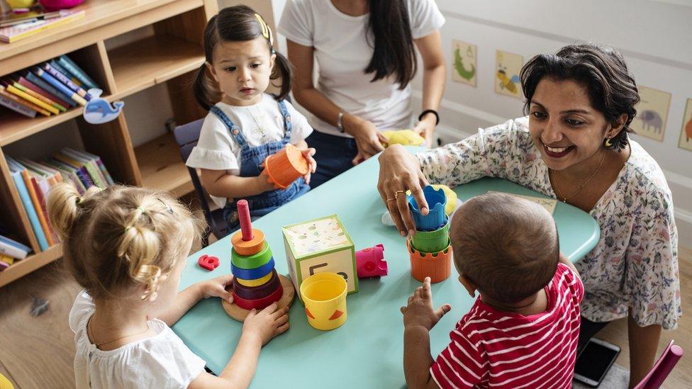 Nursery workers play with children sat around a table