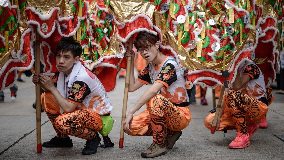 Three boys crouch on the ground, holding up part of a puppet dragon in the streets of Hong Kong.