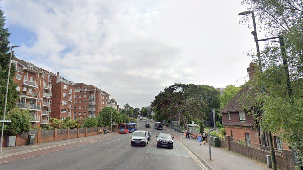 The four-lane A35 with flats on one side and cars waiting at traffic lights