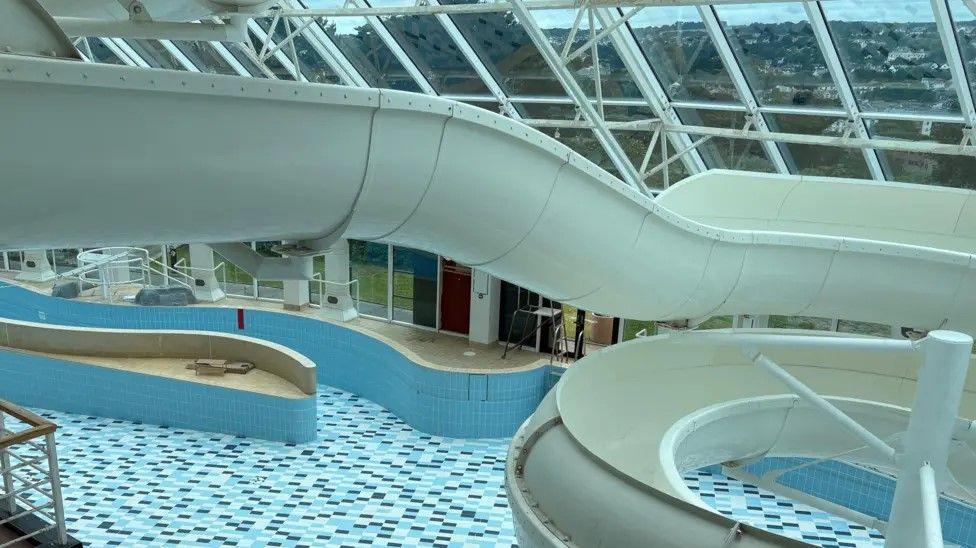 Looking down at the un-used pool at Ships & Castles with the water chute in the foreground and the empty tiled bottom of the pool beneath.