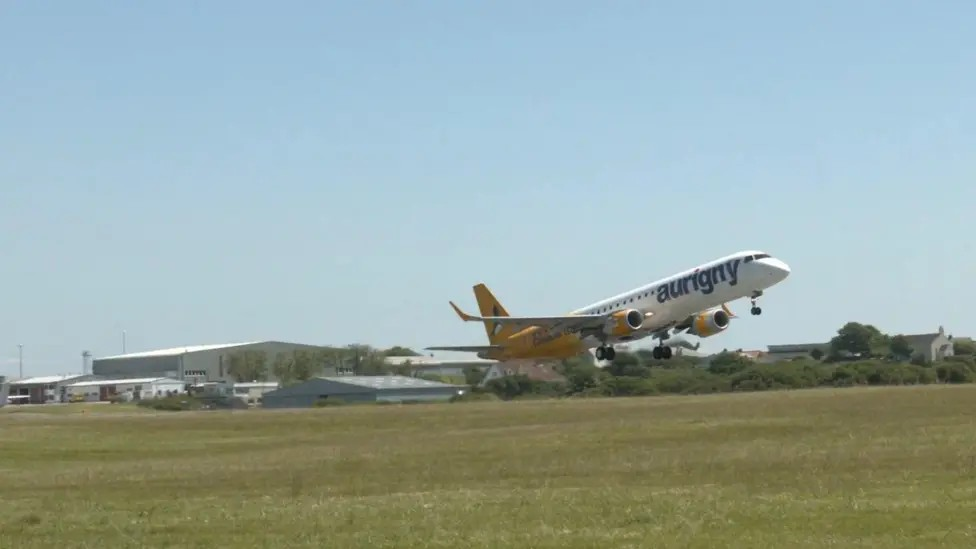 An yellow and white Aurigny jet plane takes off from Guernsey airport on a sunny day.