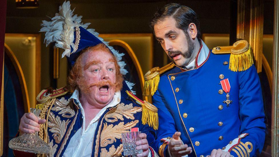 Les Dennis wearing false ginger moustache, sideburns and hair, and a decorative naval uniform and hat, alongside co-star John Savournin in a blue uniform during a dress rehearsal of HMS Pinafore