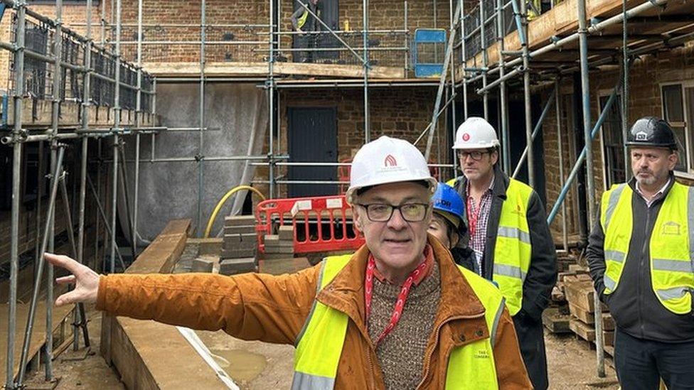 Old derelict building surrounded by scaffolding and four men in hard hats