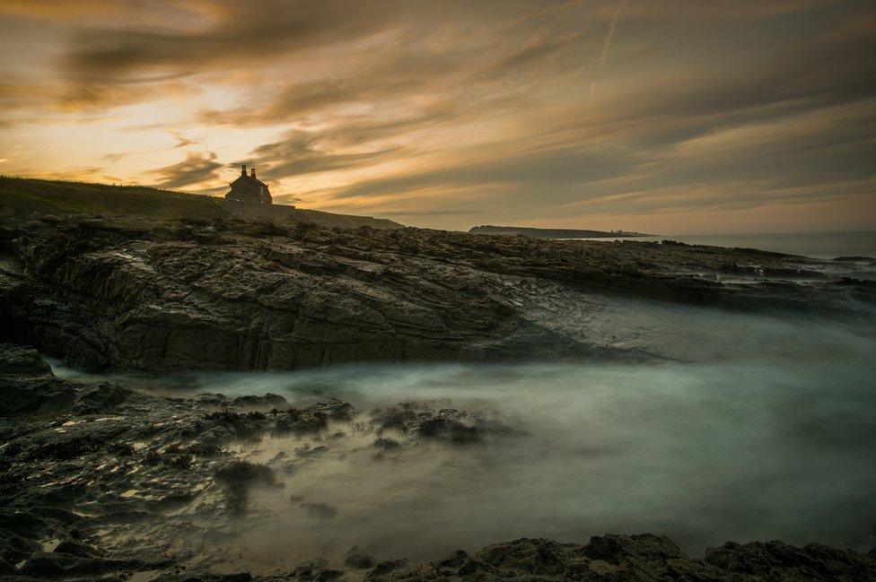 House on clifftop above long exposure sea