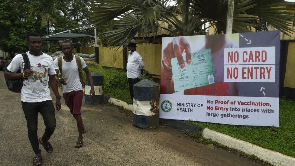 Young men walking past a poster warning that you need proof of vaccination to enter