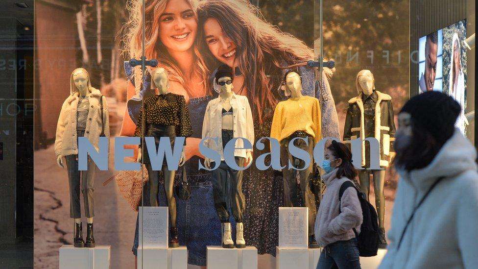 people wearing masks walk past a Topshop shop window