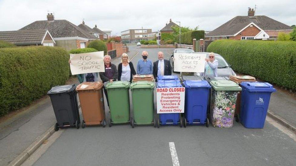 People lined up on a street with wheelie bins