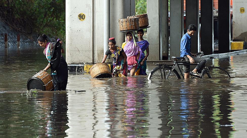 Indian pedestrians and a cyclist wade through a flooded street after heavy monsoon rain showers in Mumbai on June 21, 2016