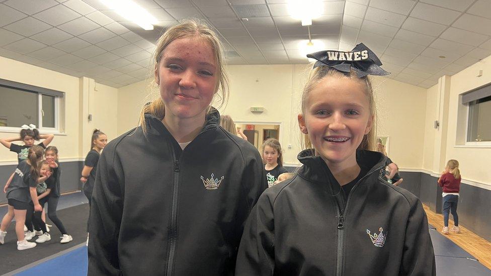 Two gymnasts smiling at the camera in training clothes in village hall