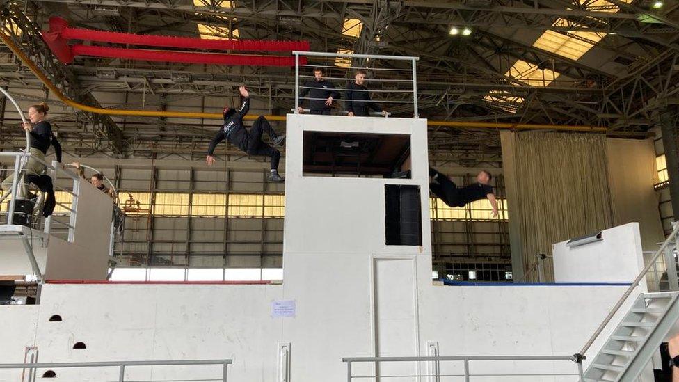 Trampolinists jumping off a high platform onto a trampoline. Two artists are in the air.