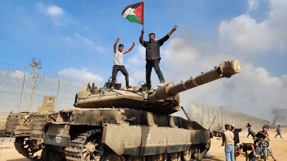 Gazans stand on top of a destroyed Israeli tank in Gaza