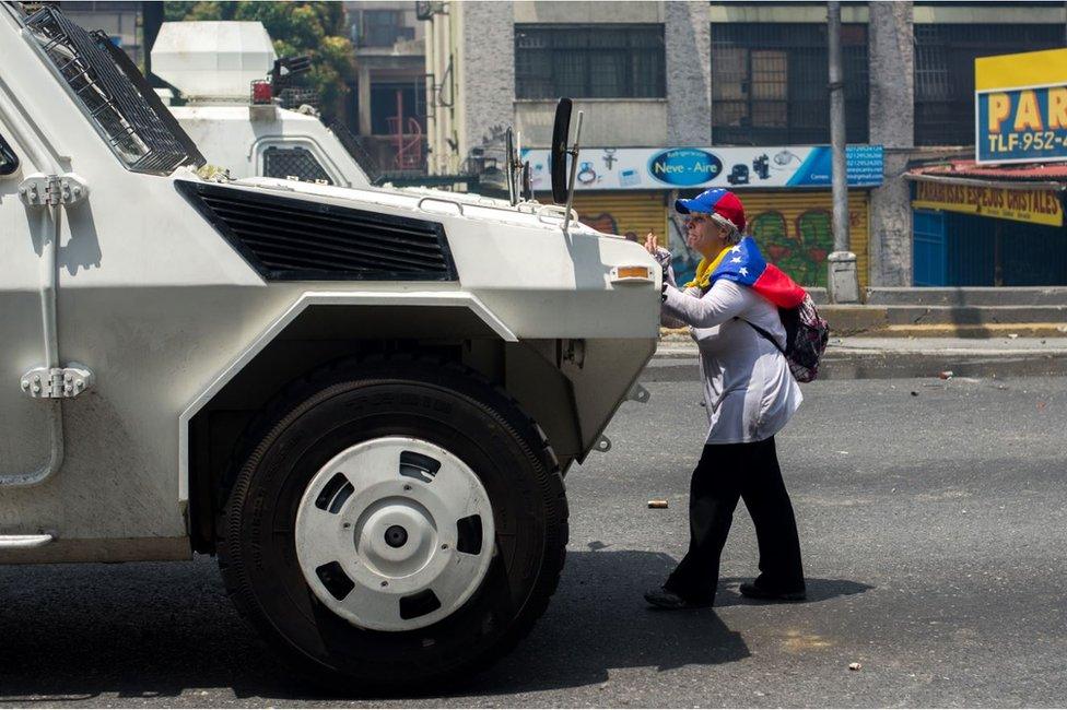 A woman stands in front of a vehicle of the Venezuelan security forces on 19 April 2017