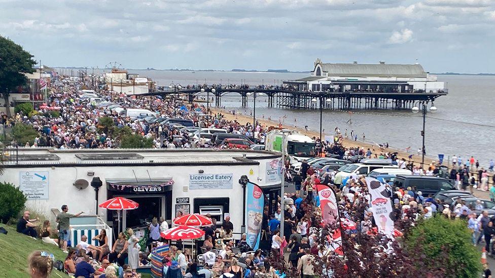 Crowds of people along Cleethorpes Promenade during last year's Armed Forces with the pier in the background and a single storey, white walled cafe in the foreground