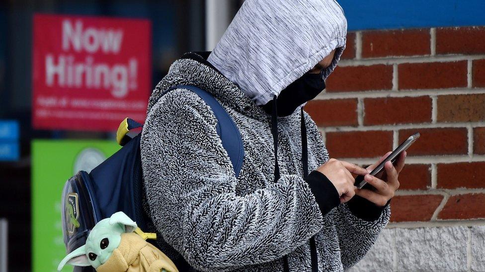 a person in a mask near a now hiring sign