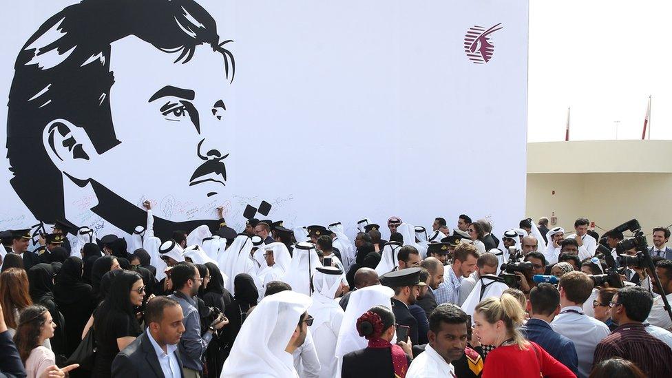 Qatar Airways workers stand in front of a wall bearing a portrait of Qatari Emir Sheikh Tamim bin Hamad Al Thani in support of the country and its leader in Doha. 13 July 2017