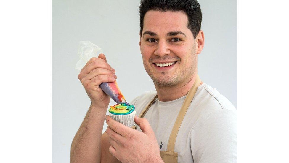 Luke smiles while icing a rainbow cupcake