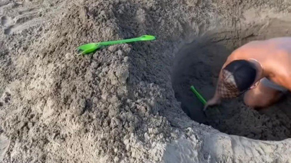 Man digging a hole on a beach.