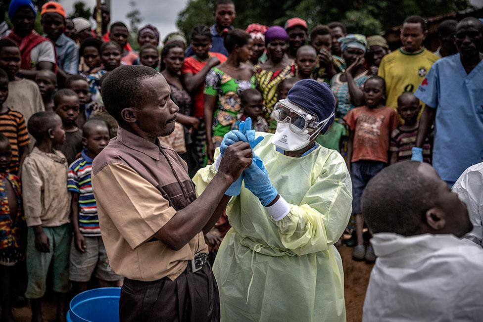 A Red Cross burial worker shows a man how to put on protective gloves