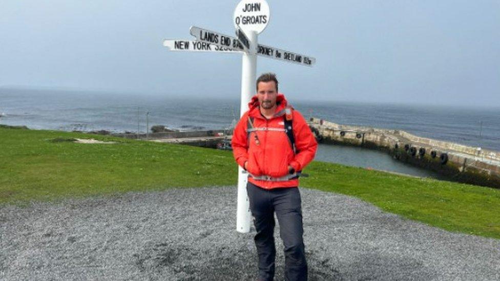 George Bromley stood in front of a signpost in John O'Groats