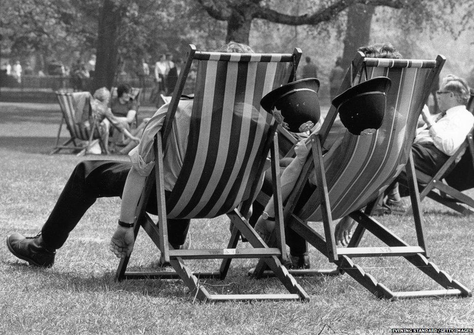 Two London policemen take the weight off their feet during the May heatwave, while patrolling in the park