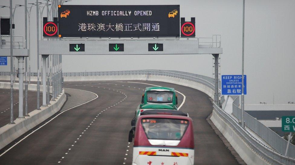 Buses drive past a sign on the Hong Kong-Zhuhai-Macau Bridge offshore in Hong Kong