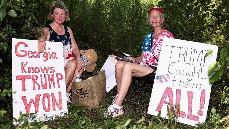 Marsha and Cathy, supporters of former US President Donald Trump, rest in a shade near the entrance of the Fulton County Jail