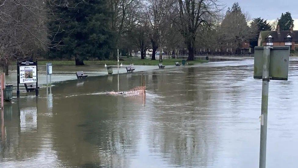 A road in Abingdon submerged under several inches of water. At the edge of the water are benches and bins.