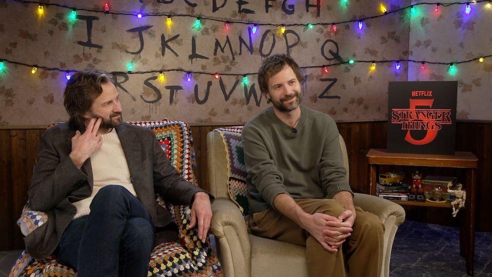 The Duffer Brothers sat together next to a Stranger Things 5 sign