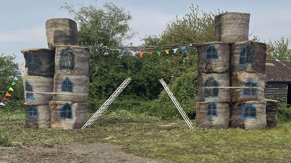 Two stacks of straw bales, painted with windows, and two ladders in between, recreating Tower Bridge, London