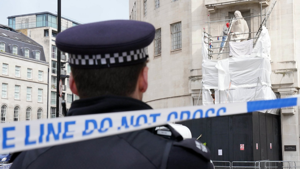 Police officer watches on as man damages statue outside BBC headquarters