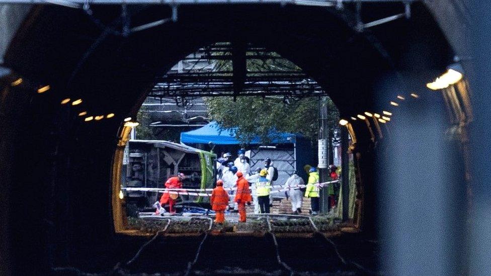 Emergency workers carry a stretcher away from an overturned tram