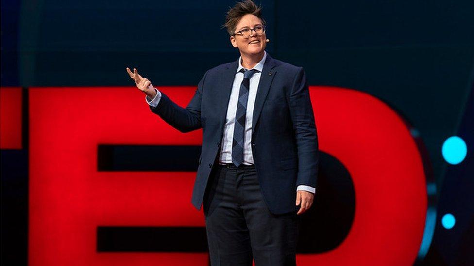 A woman in glasses stands in front of a sign that reads 'TED'