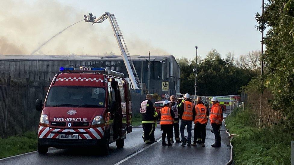 Firefighters in front of a large building with smoke rising from it