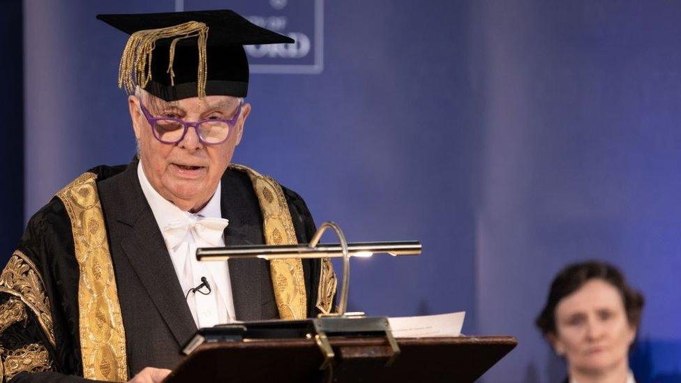 Lord Patten speaking at a lectern with Prof Irene Tracey in the background