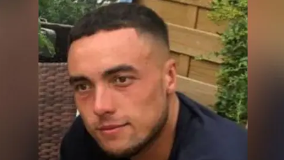 Kieran Shepherd, who has short black hair, stubble and is wearing a navy T-shirt. He is sat in front of a garden fence, looking beyond the camera.