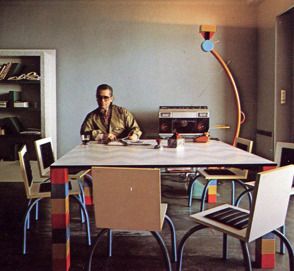 Karl Lagerfeld sitting in his Monte Carlo apartment with designs by the Memphis Group including "Pierre" table by Sowden and "Treetops" lamp by Sottsass